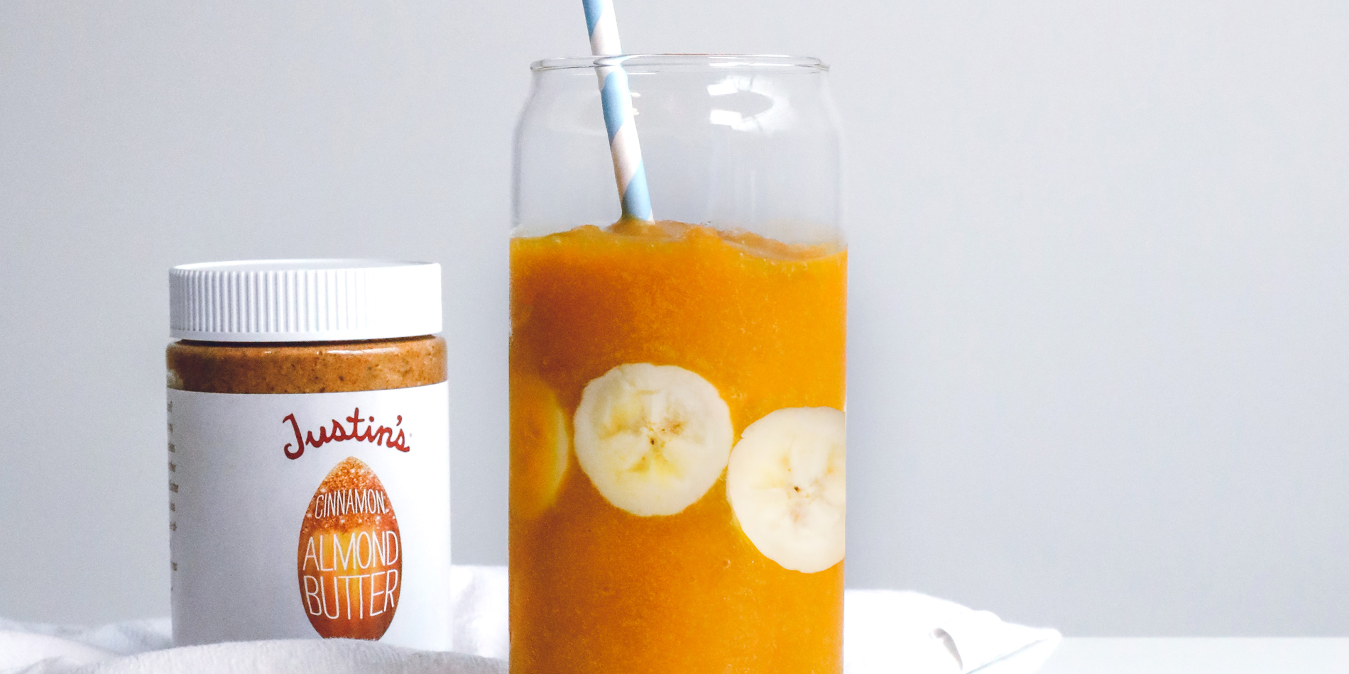 Golden Cinnamon Turmeric Smoothie with banana slices with a straw in a clear cup in a white background with a white cloth