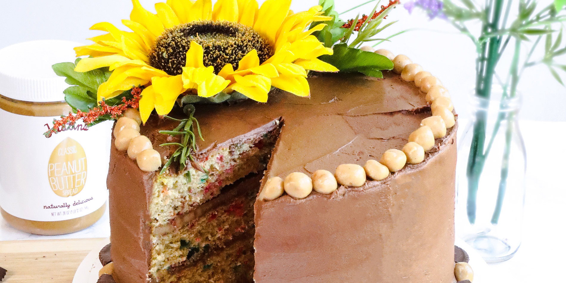 Peanut Butter Cake with Chocolate Buttercream with a sunflower on top of the main cake with a slice cut on a white plate