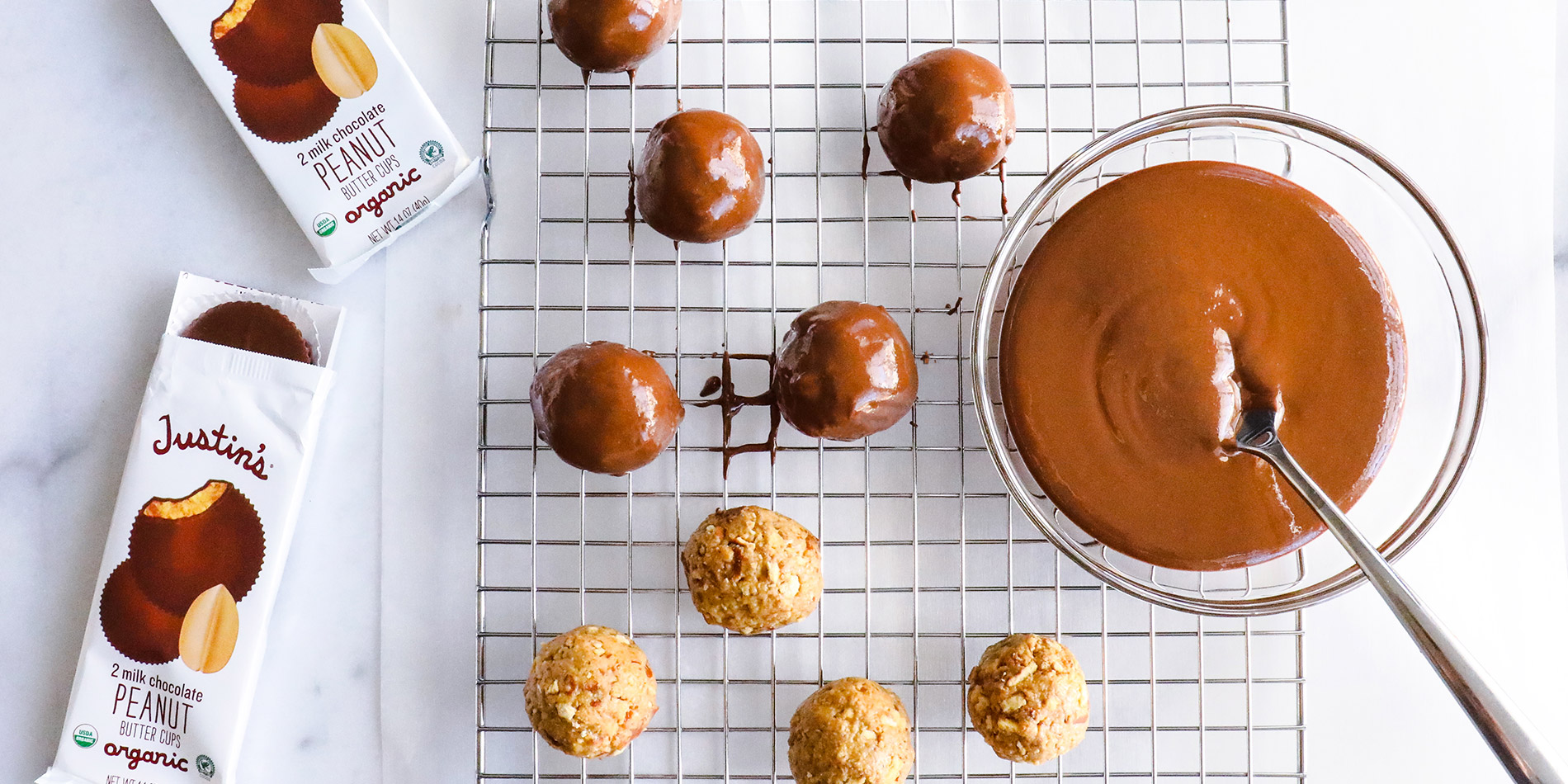 Peanut Butter Pretzel Balls on a cooling tray with 2 peanut butter cup packs on the left on a white marble background