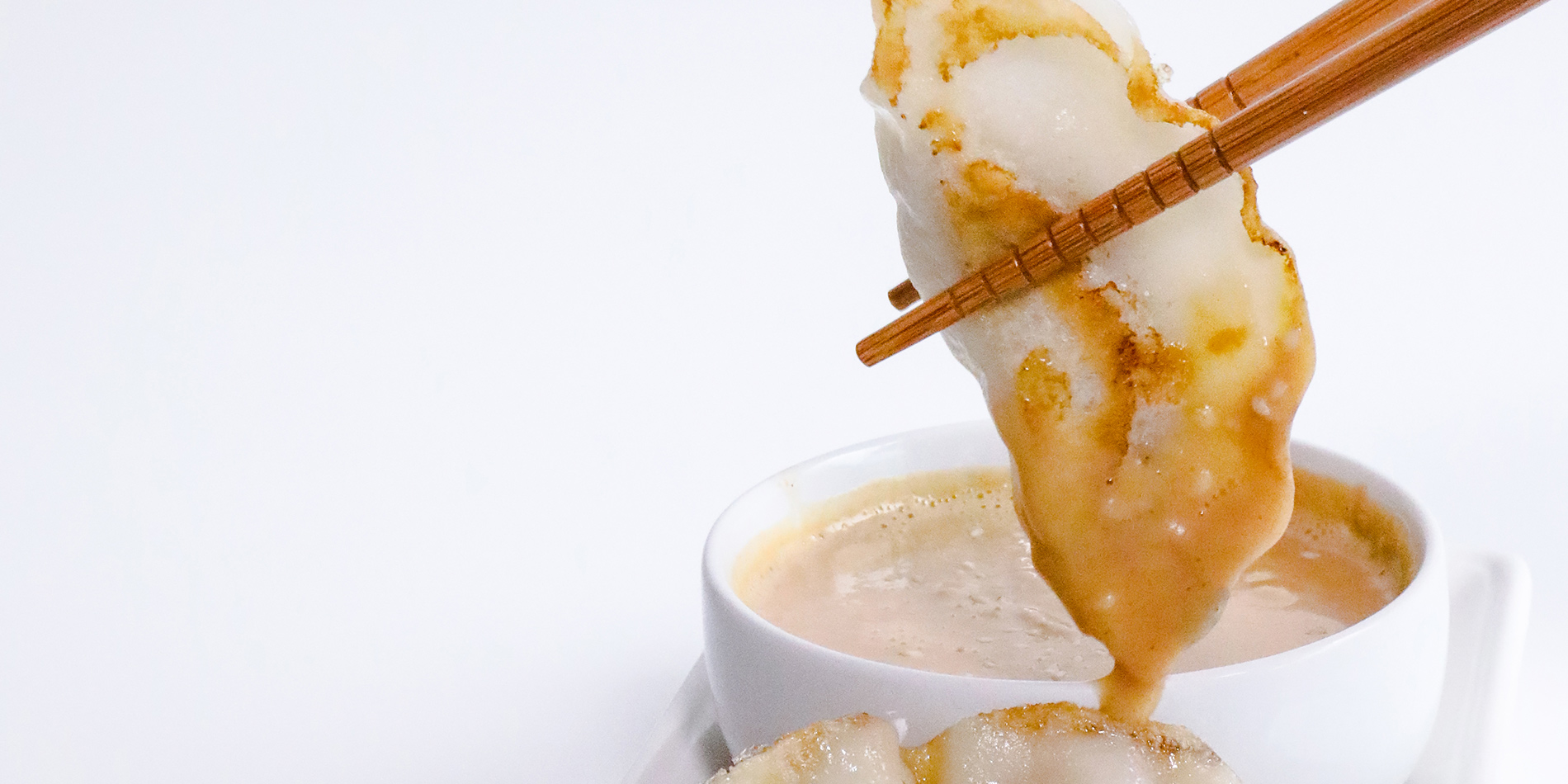 Spicy Peanut Sauce used to dip dumplings being held with brown wooden chopsticks on a white background