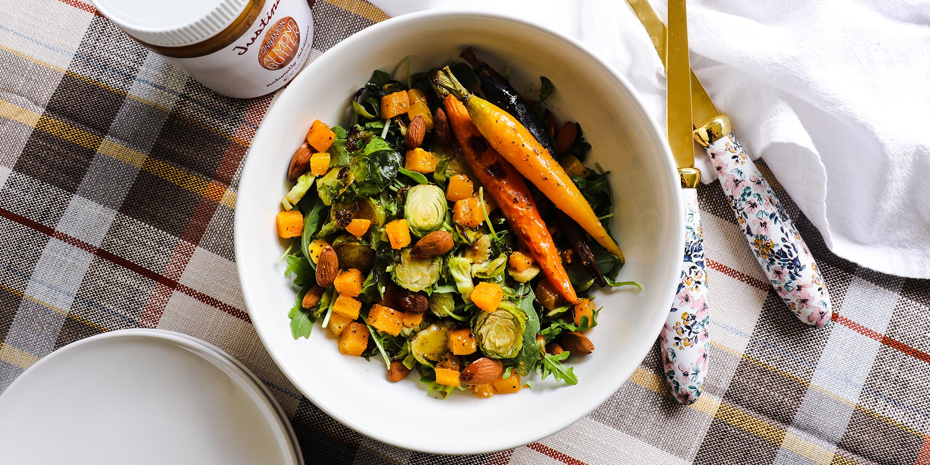 Warm Autumn Salad with Almond Butter Vinaigrette in a white bowl on a tartan pattern background with gold cutlery