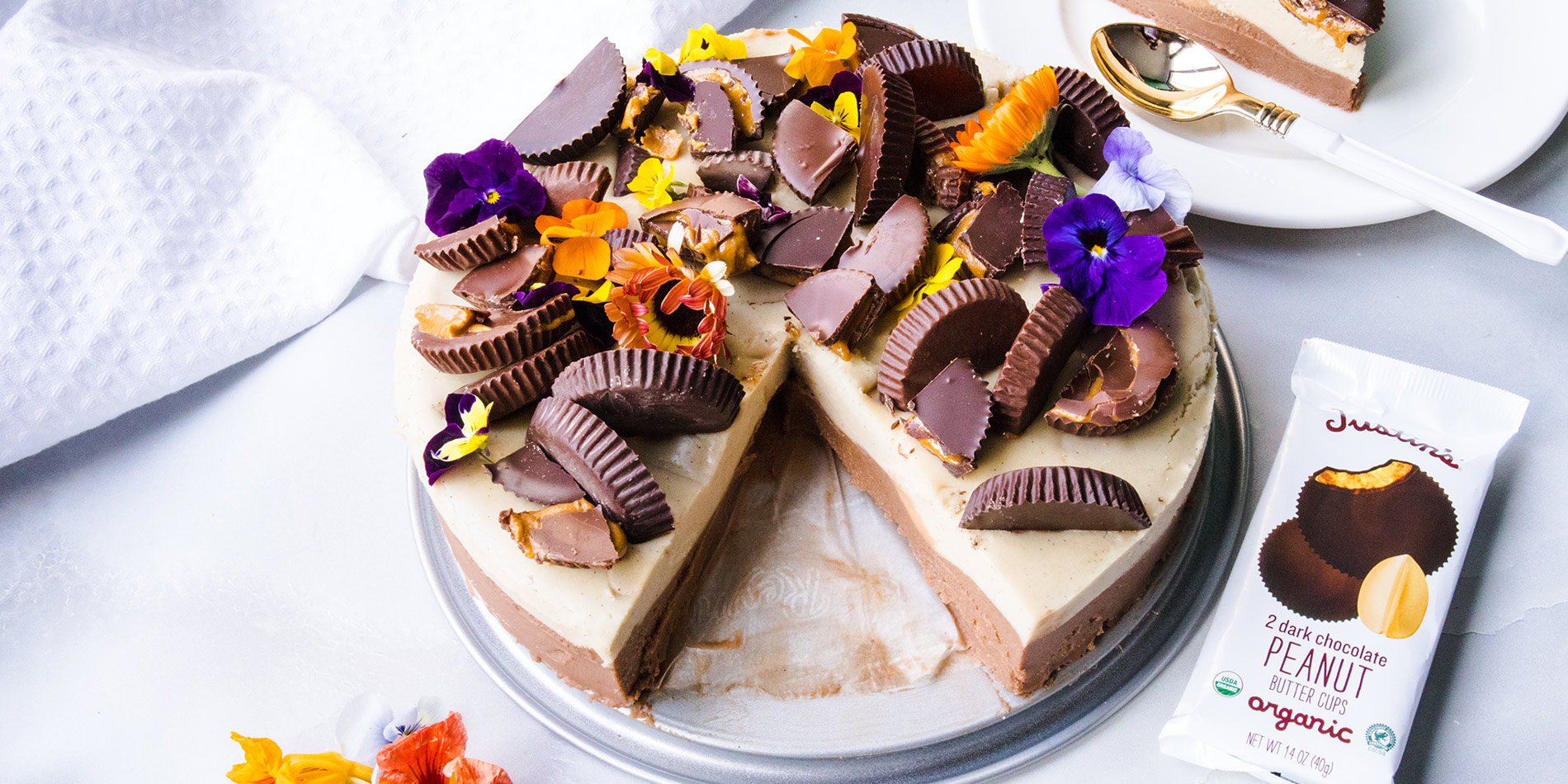 Peanut Butter Chocolate Cashew Cheesecake on a gray tray with a slice taken out and placed on top right side of the photo