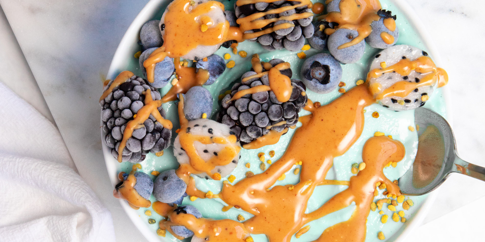 Blue Lagoon Smoothie Bowl (close up) in a white bowl with a silver spoon with white cloth underneath