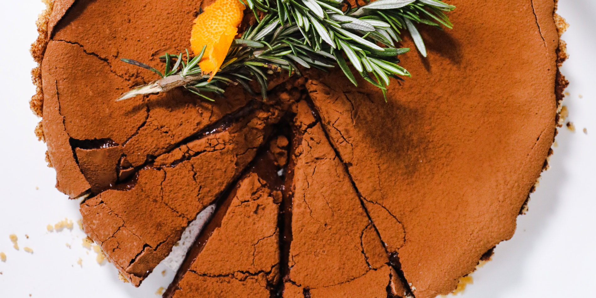 Chocolate Hazelnut Tart with Rosemary and Orange with 3 small pieces cut and still inside the tart on a white background