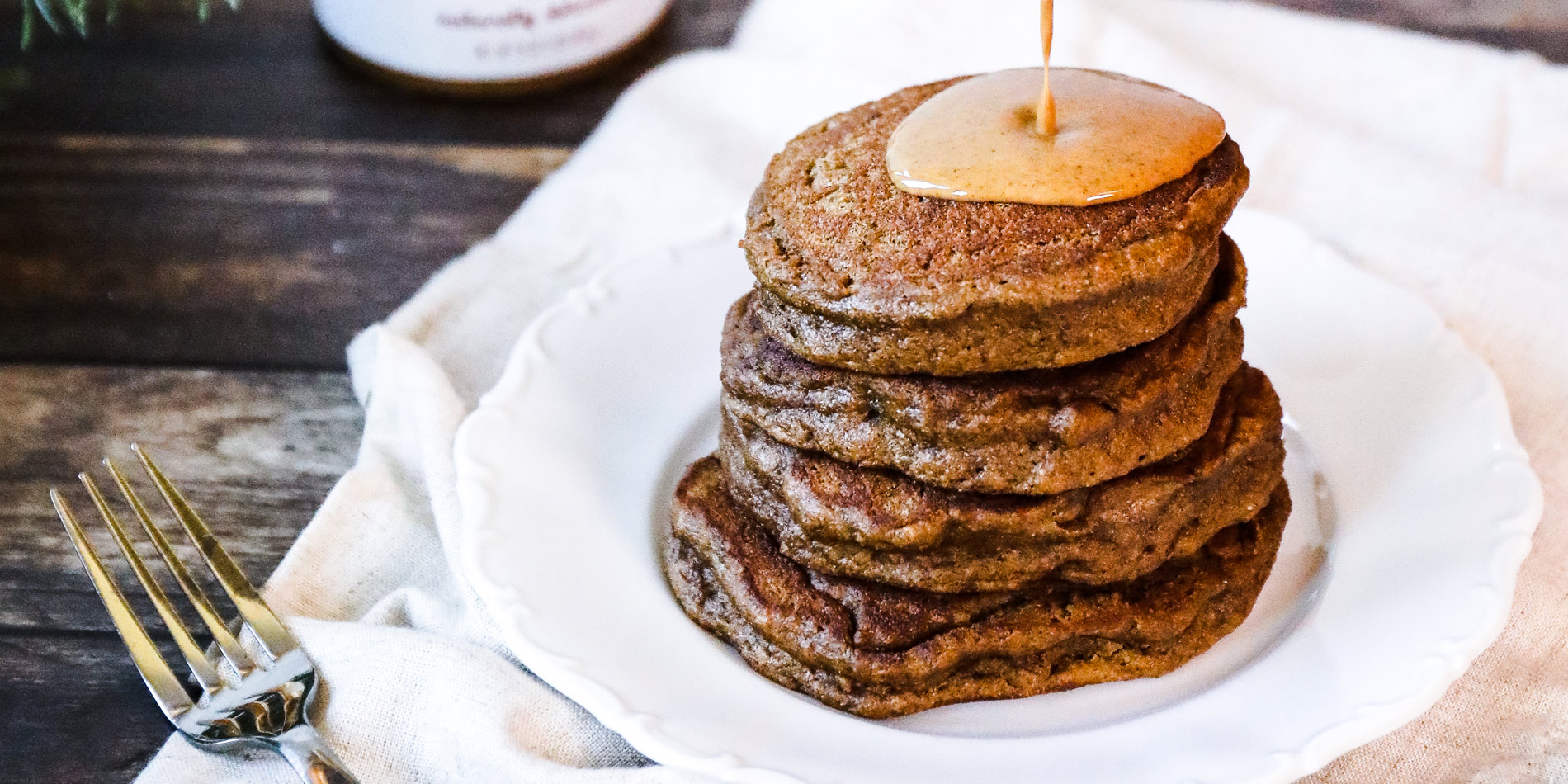 Gingerbread Almond Butter Pancakes with peanut butter drizzle on a white plate with wooden background with pine tree