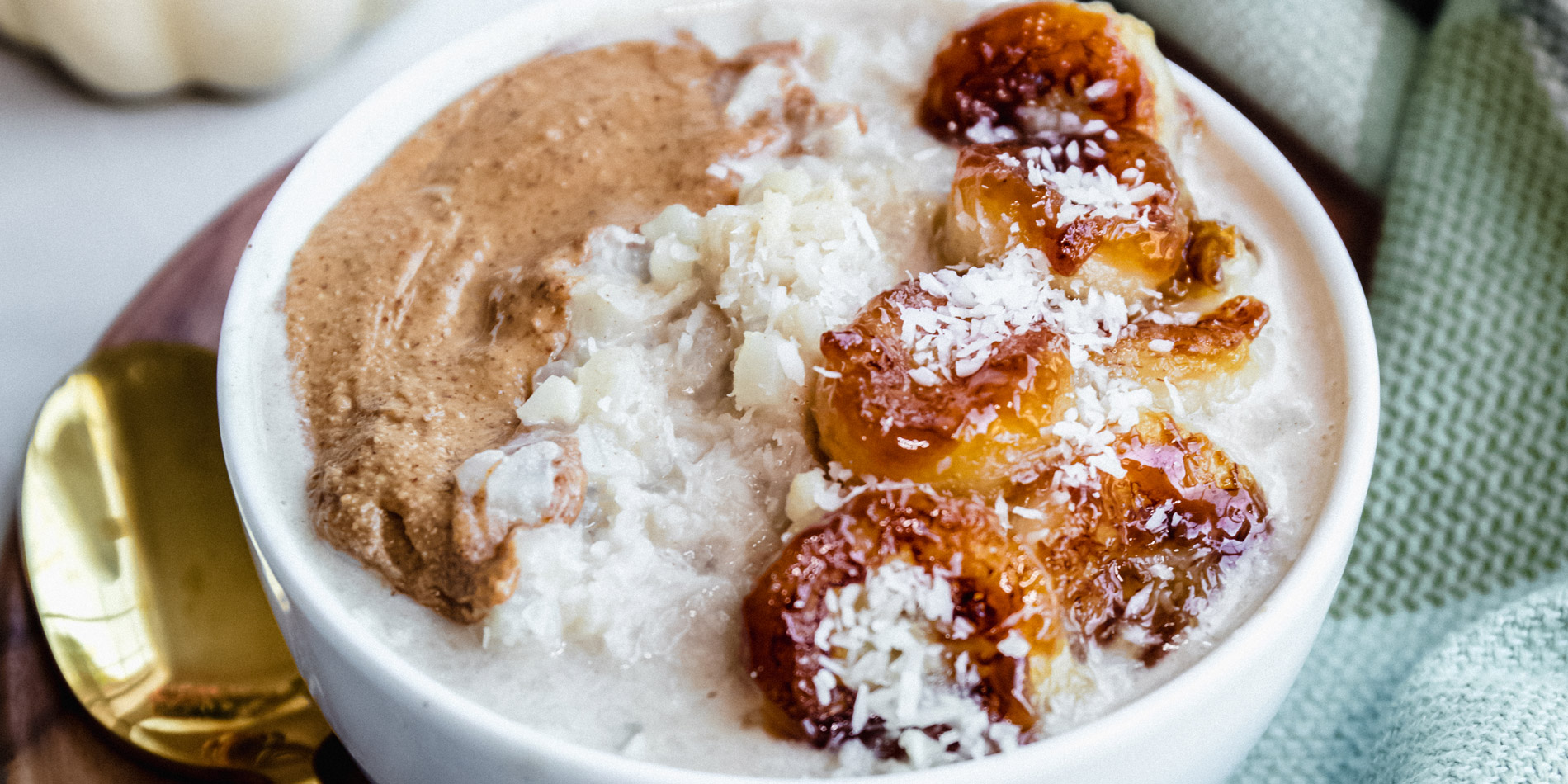 Grain Free Coconut Cauliflower Oats with Caramelized Bananas on a wood bowl with a gold spoon on a white background