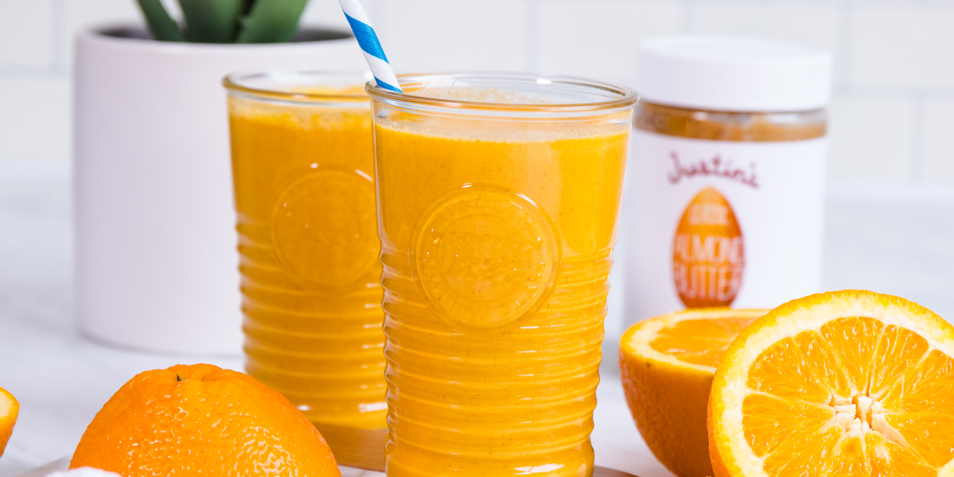 Orange Creamsicle Smoothie in tall glass cups with a white and blue straw with oranges in the background