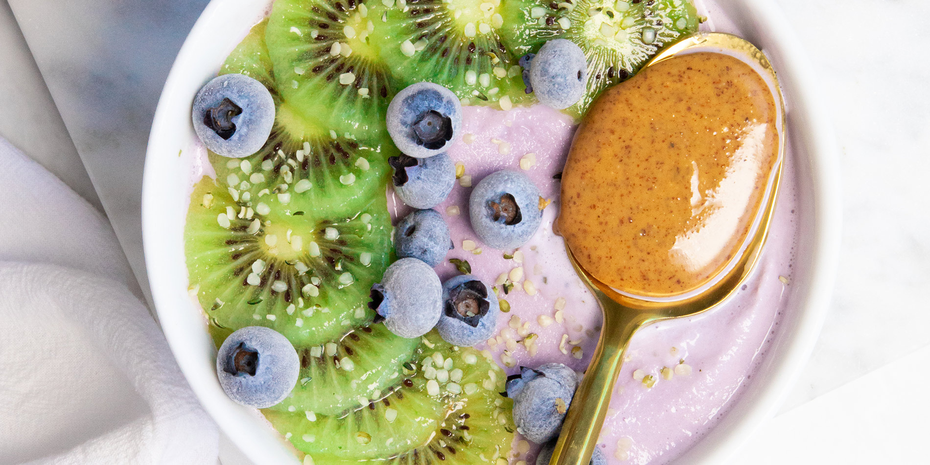 Maple Blueberry Smoothie Bowl with kiwi slices and a spoonful of Justin's Maple Almond Butter in a white marble background