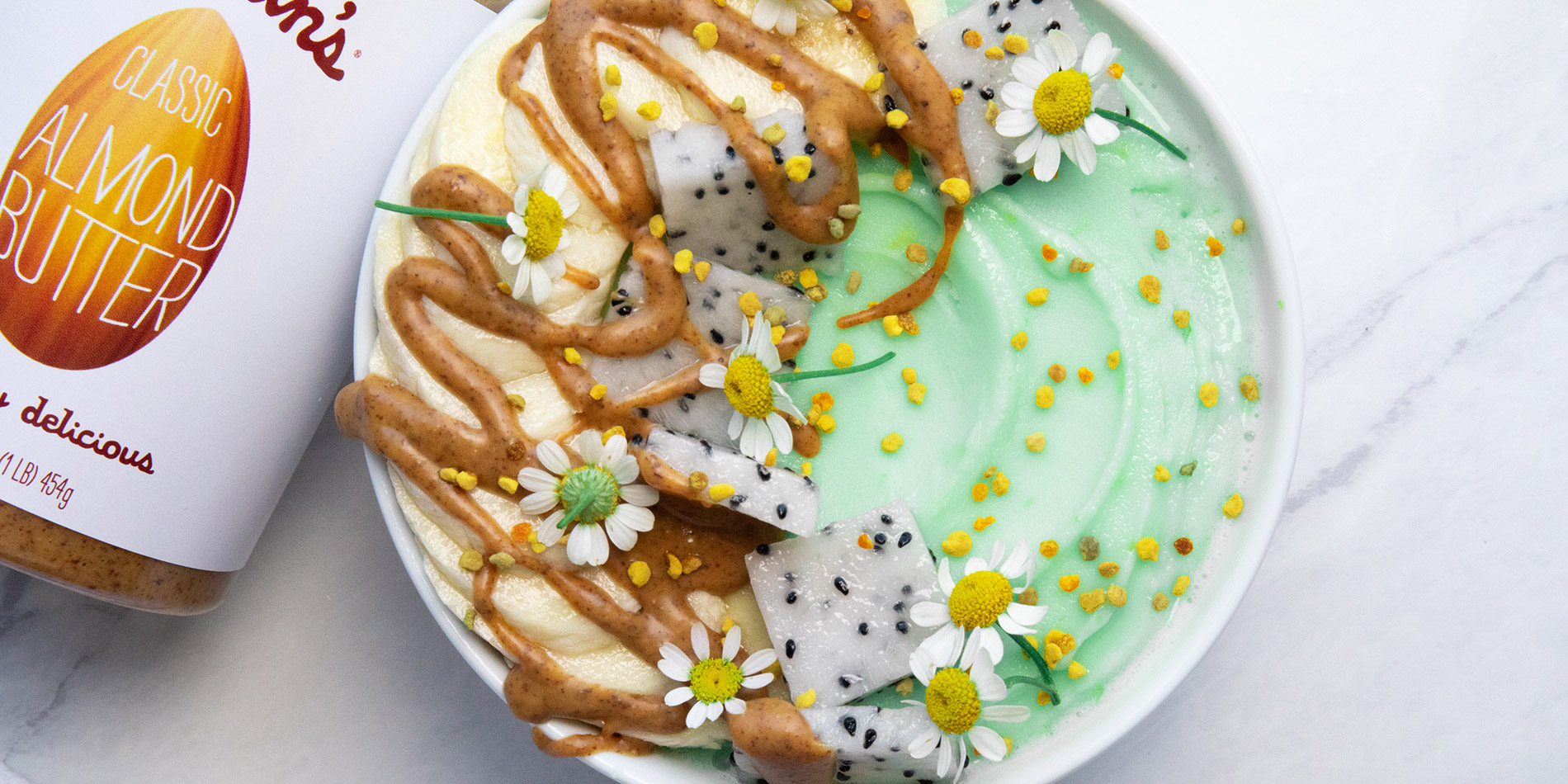 Matcha Smoothie Bowl with Justin's almond butter drizzle, flowers and sliced dragonfruit as condiments on a white background