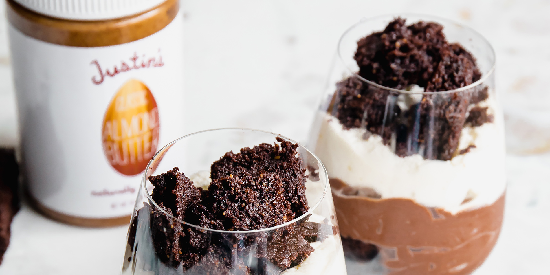 Paleo Almond Butter Brownie Parfait in clear cups with fudge chunks and crumbs on a white background