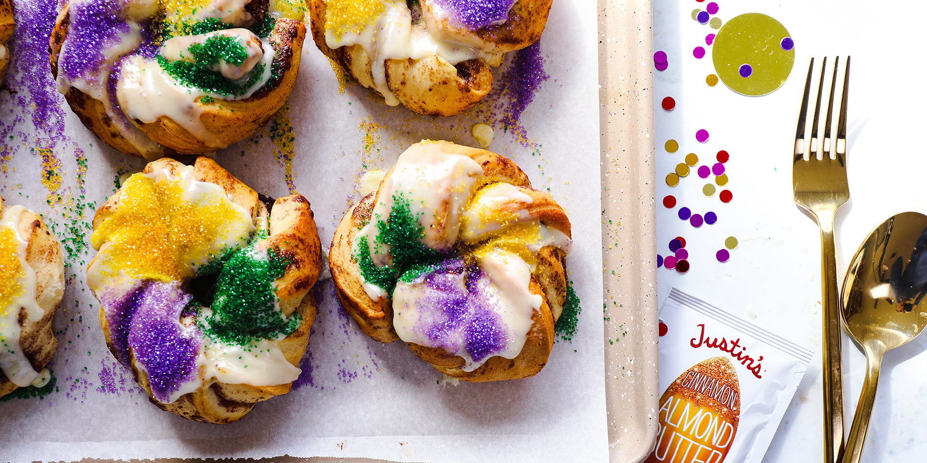 Personal Cinnamon Almond Butter King Cakes on top of a tray with parchment paper with rainbow confetti on a white background