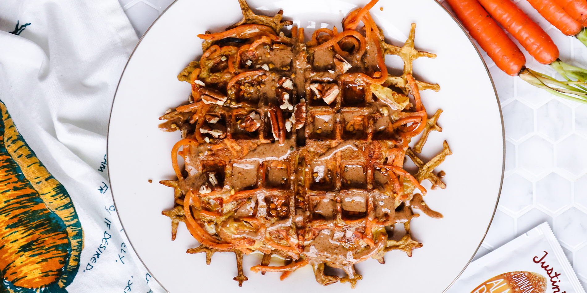 Spiralized Carrot Cake Waffle with carrots and a gold fork in the white tile background with a cloth with carrot illustration