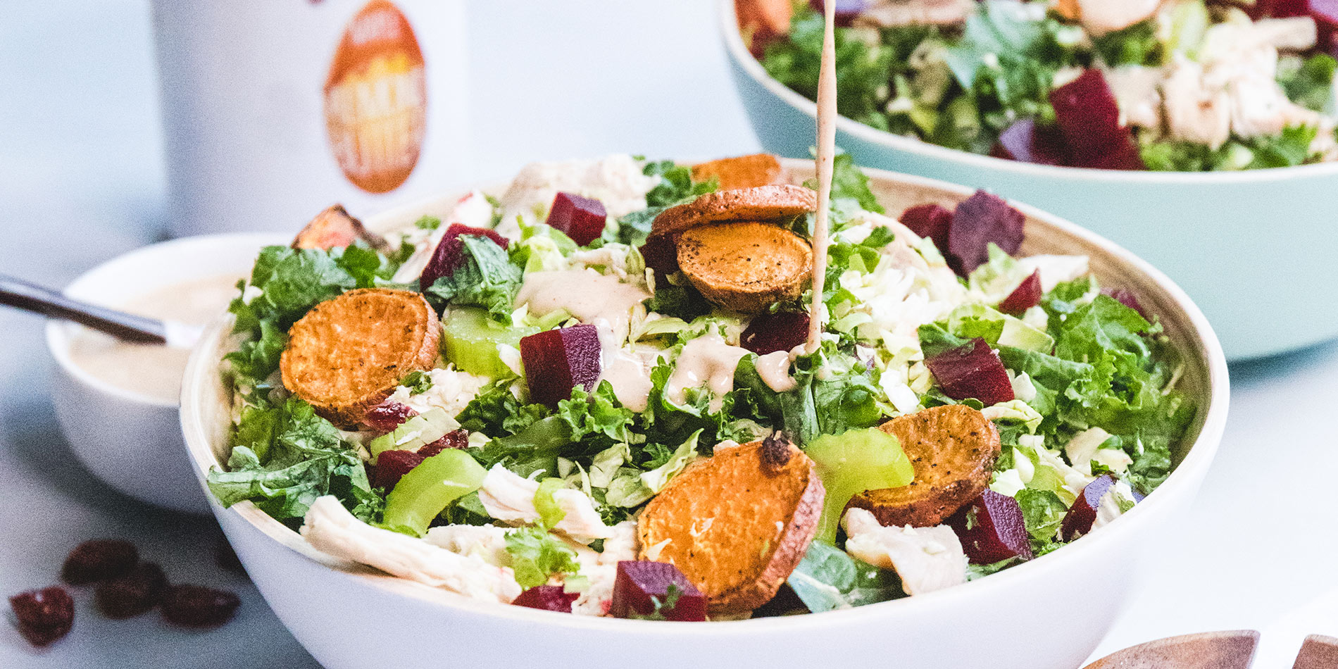 Turkey Kale and Brussels Salad with Almond Butter Tahini Dressing in a white bowl with dressing sauce poured from above