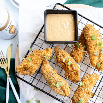Pretzel Crusted Chicken Tenders with Maple Almond Dijon Dipping Sauce on a black cooling rack on top of a round wooden tray thumbnail image