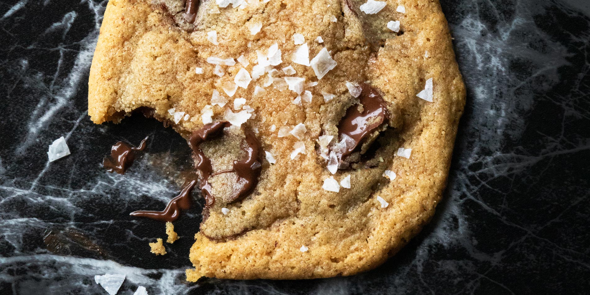 Almond Butter Tahini Chocolate Chip Cookie bitten into, and placed on a black marble tabletop