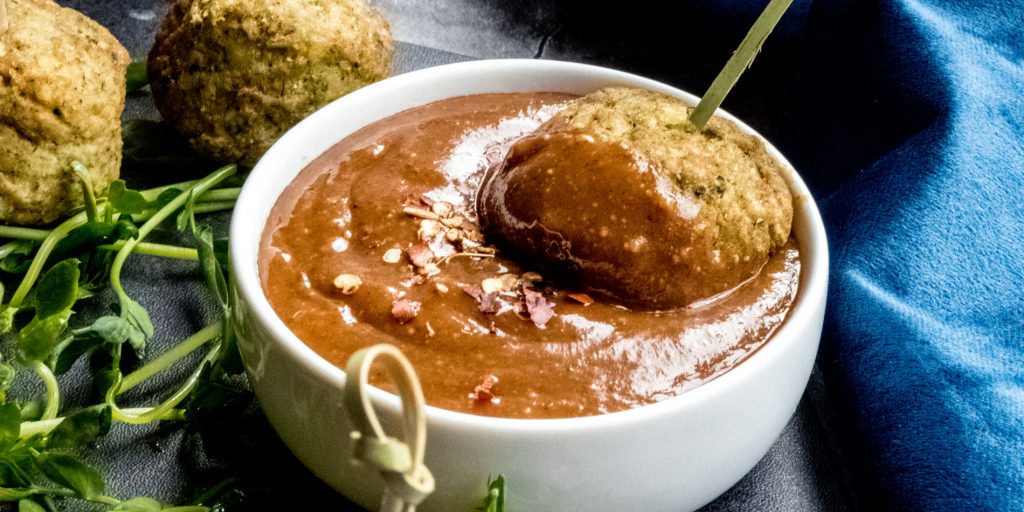 Balsamic Almond Butter Dipping Sauce dipped with meatballs in a small round white bowl against a blue fabric background