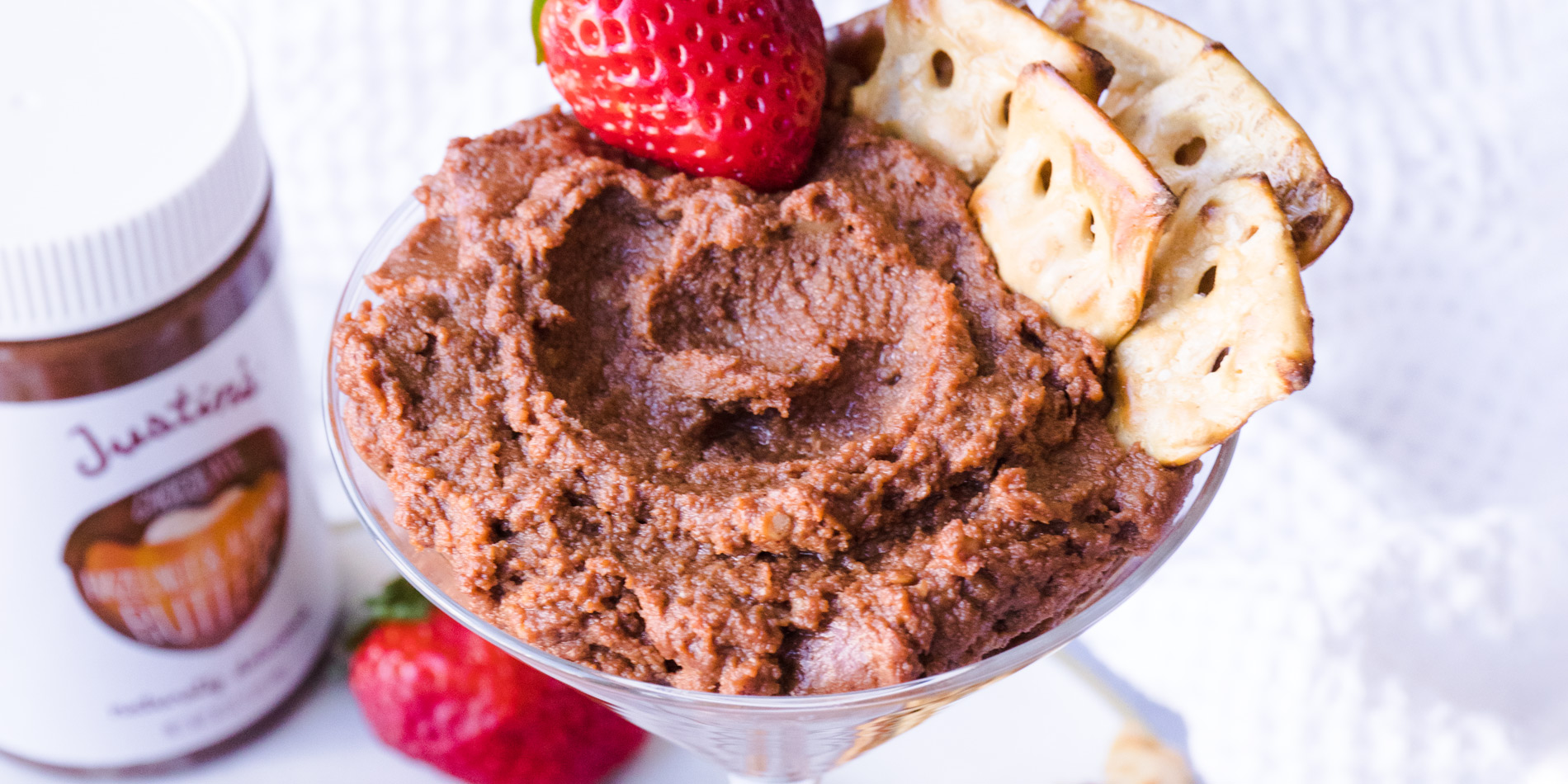 Chocolate Hazelnut and Almond Dessert Hummus on a clear glass with strawberries in the background