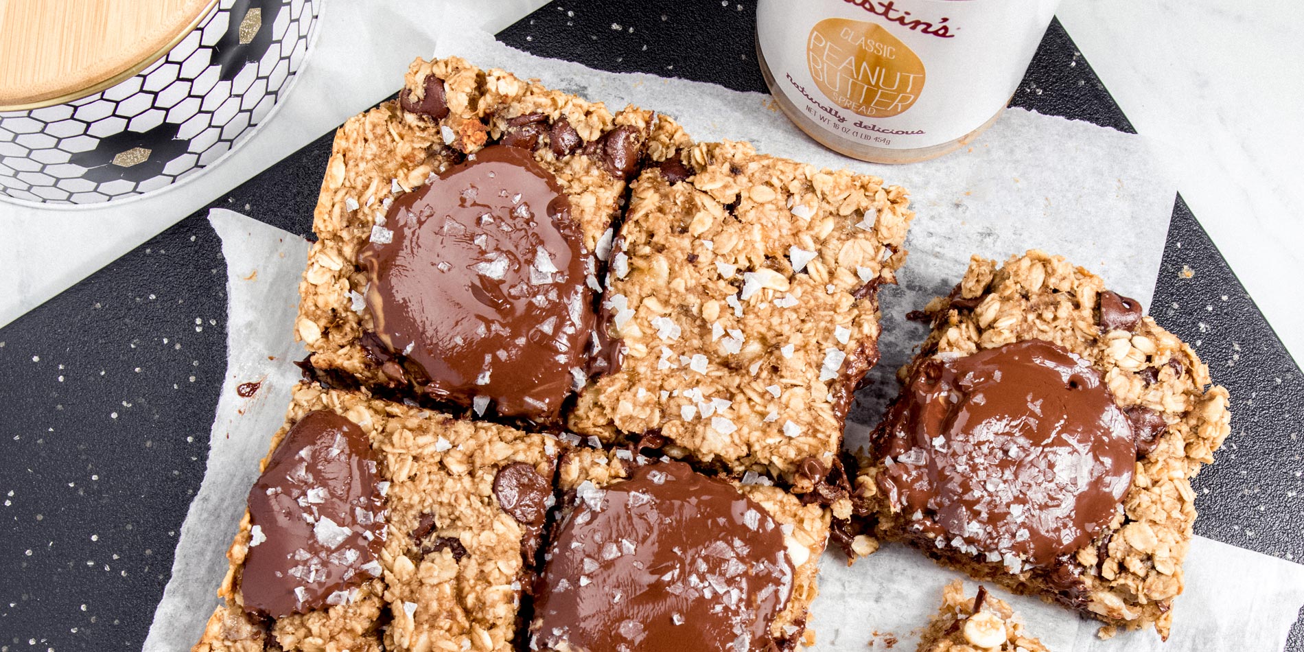 Chocolate Peanut Butter and Banana Oatmeal Cookie Bars on parchment papers on a black rectangular tray on a white background