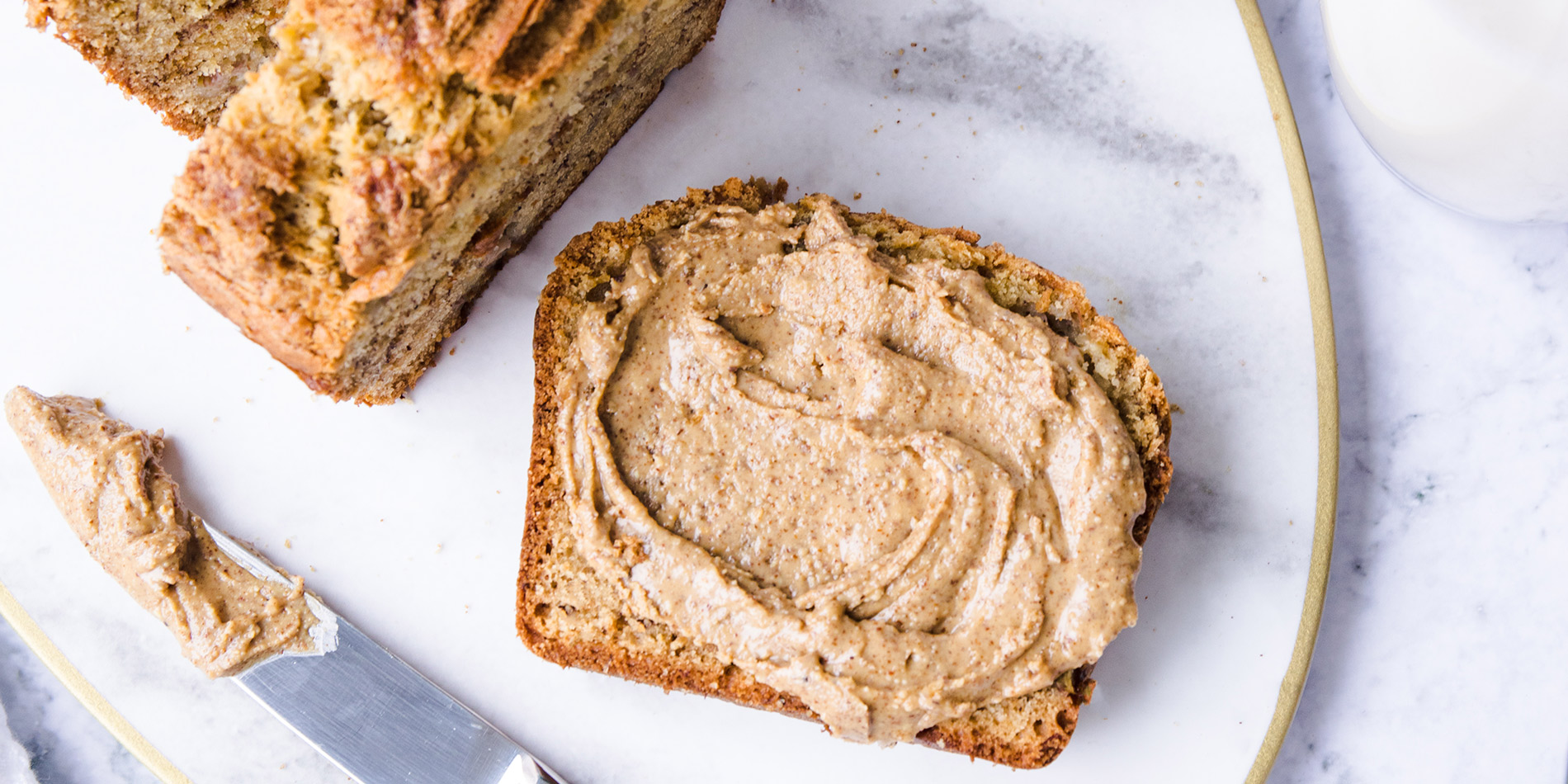 Cinnamon Almond Swirl Banana Bread on a white plate with silver cutlery on a white background