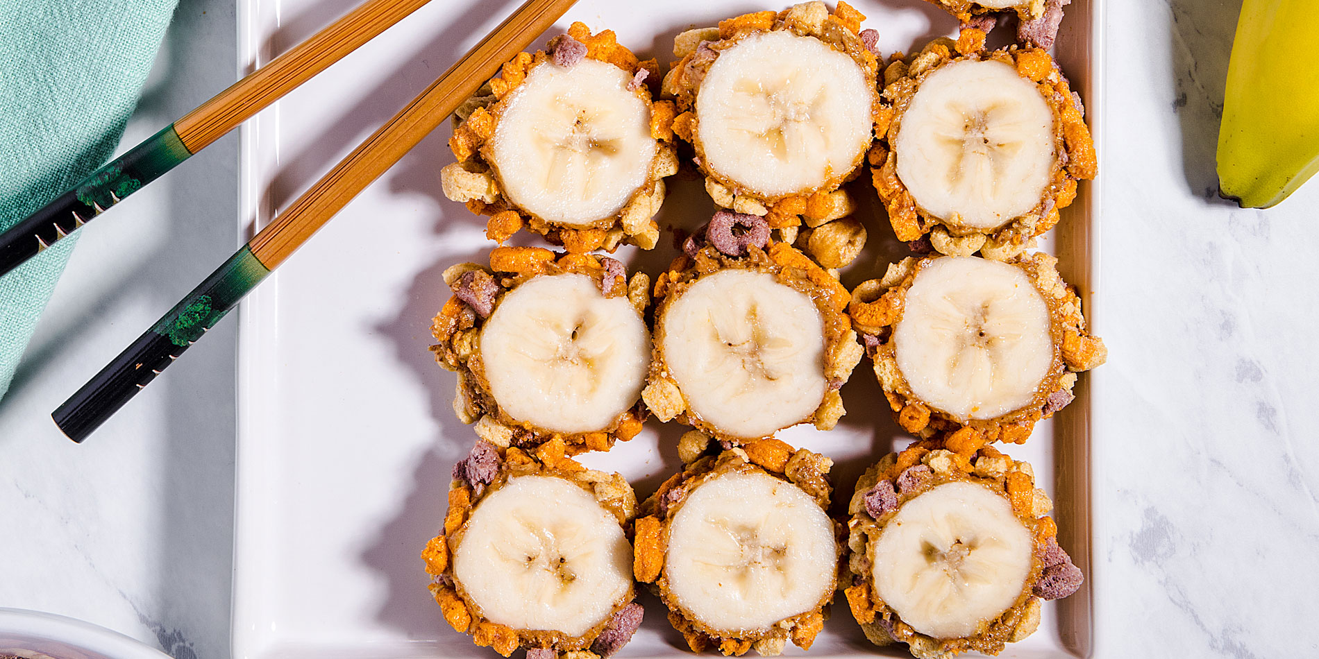 Crunchy Banana Roll on a white, rectangular plate with wooden chopsticks on top with a banana on the top right corner