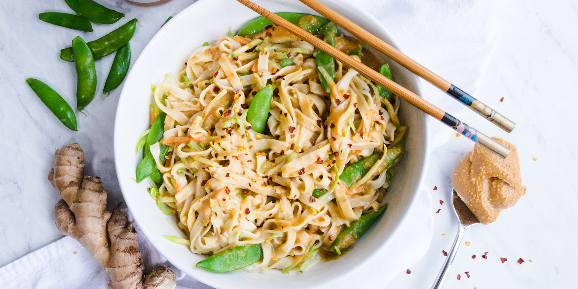 Easy Peanut-Ginger Noodles in a round white bowl with wooden chopsticks with fresh ginger in the background