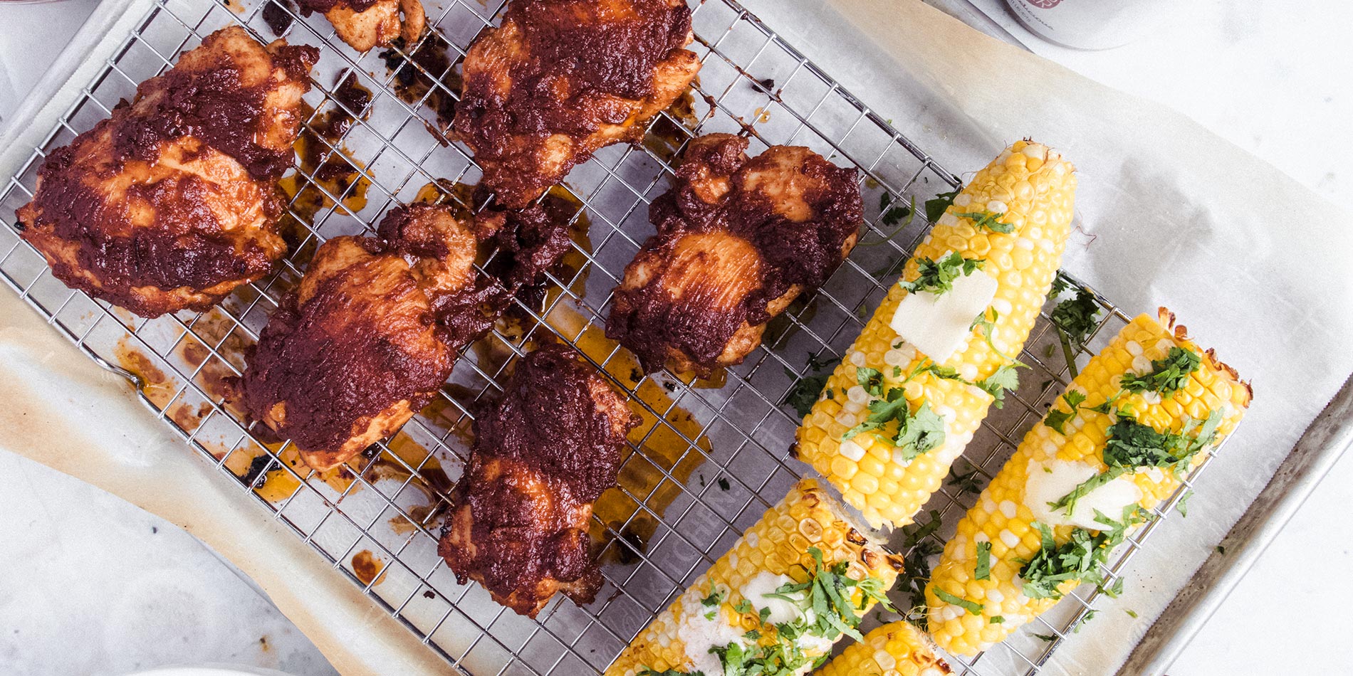 Maple Almond Barbecue Chicken beside some corn on the cob on a cooling rack in a tray with parchment paper