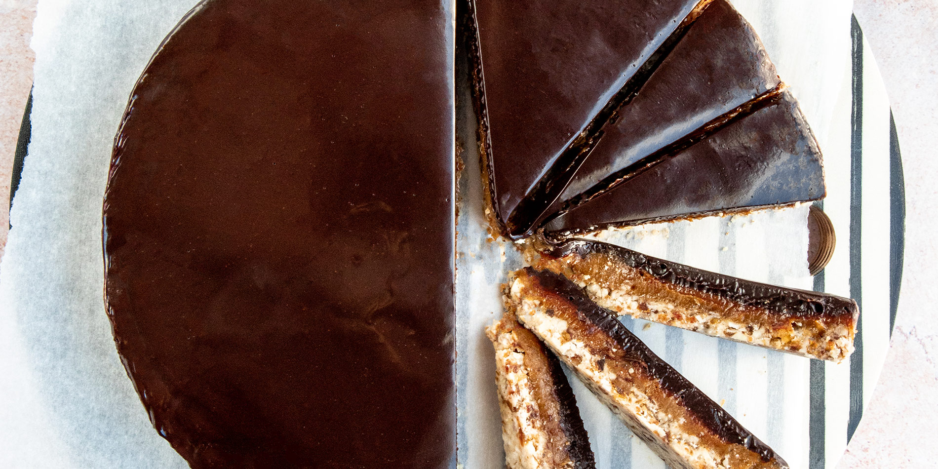 Almond Caramel Tart sliced and rotated for display over parchment, on a striped tabletop