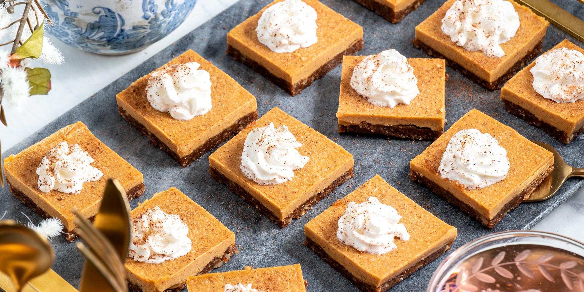 Raw Maple Almond Pumpkin Pie Bars picked up by a golden spatula from a dark gray, rectangular stone plate