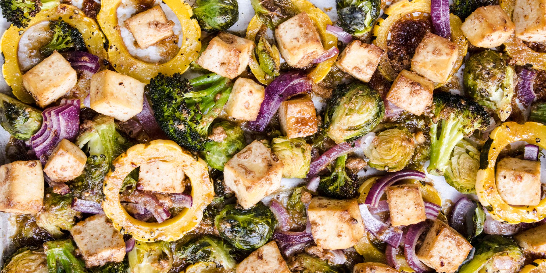 Roasted Almond Butter and Maple Glazed Tofu, Squash and Brussels in a close up shot laid on white parchment paper