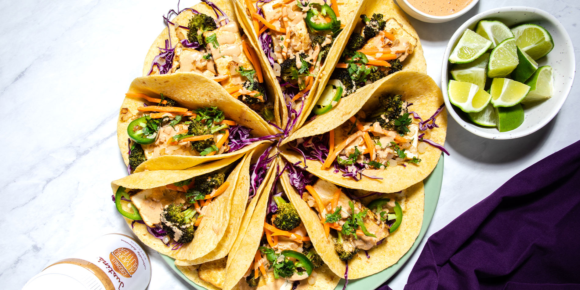 Vegan Tacos with Seared Tofu, Veggies with Spicy Coconut Almond Sauce beside a bowl of cut limes on a white marble tabletop