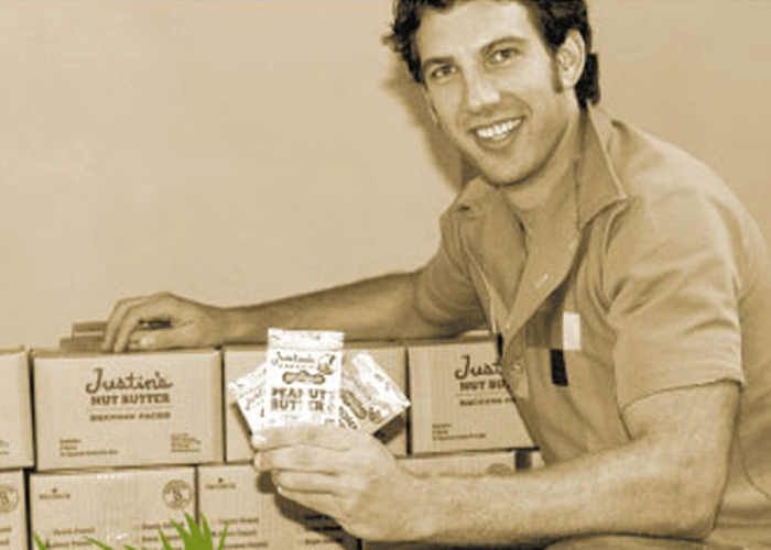 Sepia-toned photo of Justin holding packets of Justin's peanut butter spread squeeze pack with its initial package design