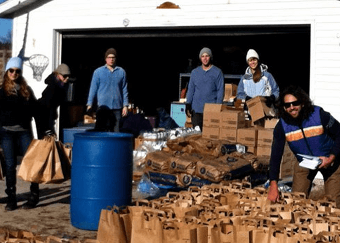 Justin and other people in front of lots of packaged products laid on the floor in front of a garage