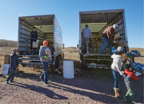 Workers moving parcels out of two big trucks on a sunny day in the middle of a grass field