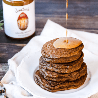 Gingerbread Almond Butter Pancakes with peanut butter drizzle on a white plate with wooden background with pine tree