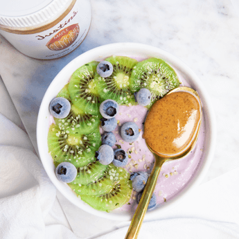 Maple Blueberry Smoothie Bowl with kiwi slices and a spoonful of Justin's Maple Almond Butter in a white marble background