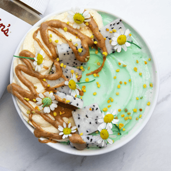 Matcha Smoothie Bowl with Justin's almond butter drizzle, flowers and sliced dragonfruit as condiments on a white background