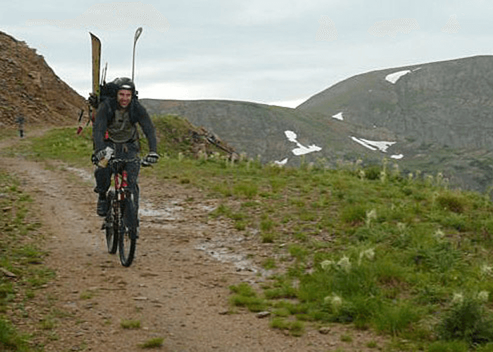 Outdoor shot of Justin with a backpack, riding a bike on a mountain trail