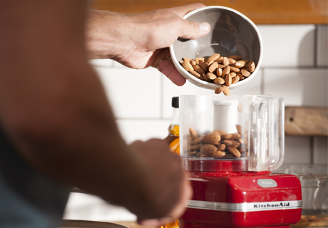 Hand pouring almonds from a bowl into a red Kitchen Aid mixer