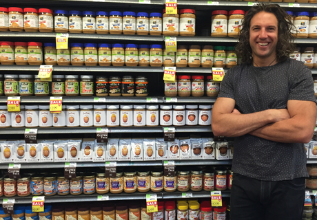 Smiling Justin with arms crossed in front of a shelf full of his products at a grocery store