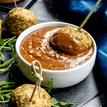 Balsamic Almond Butter Dipping Sauce dipped with meatballs in a small round white bowl against a blue fabric background thumbnail image