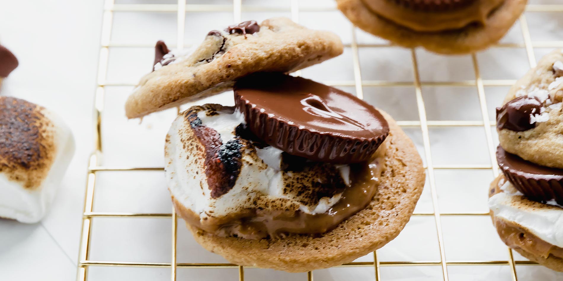 Chocolate Peanut Butter Cup Cookie S'mores laid out on gold cooking rack, atop white countertop