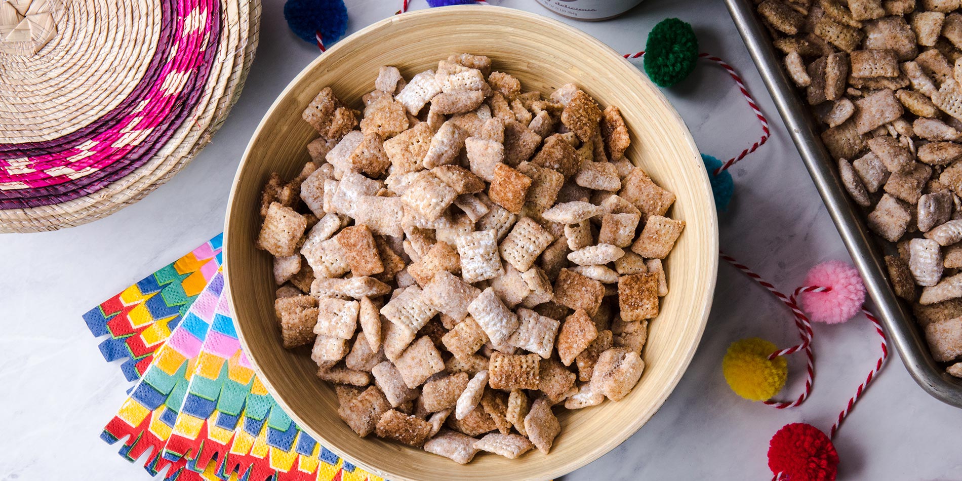 Bowl filled with Almond Butter Churro Puppy Chow atop marble countertop with decorative paper underneath