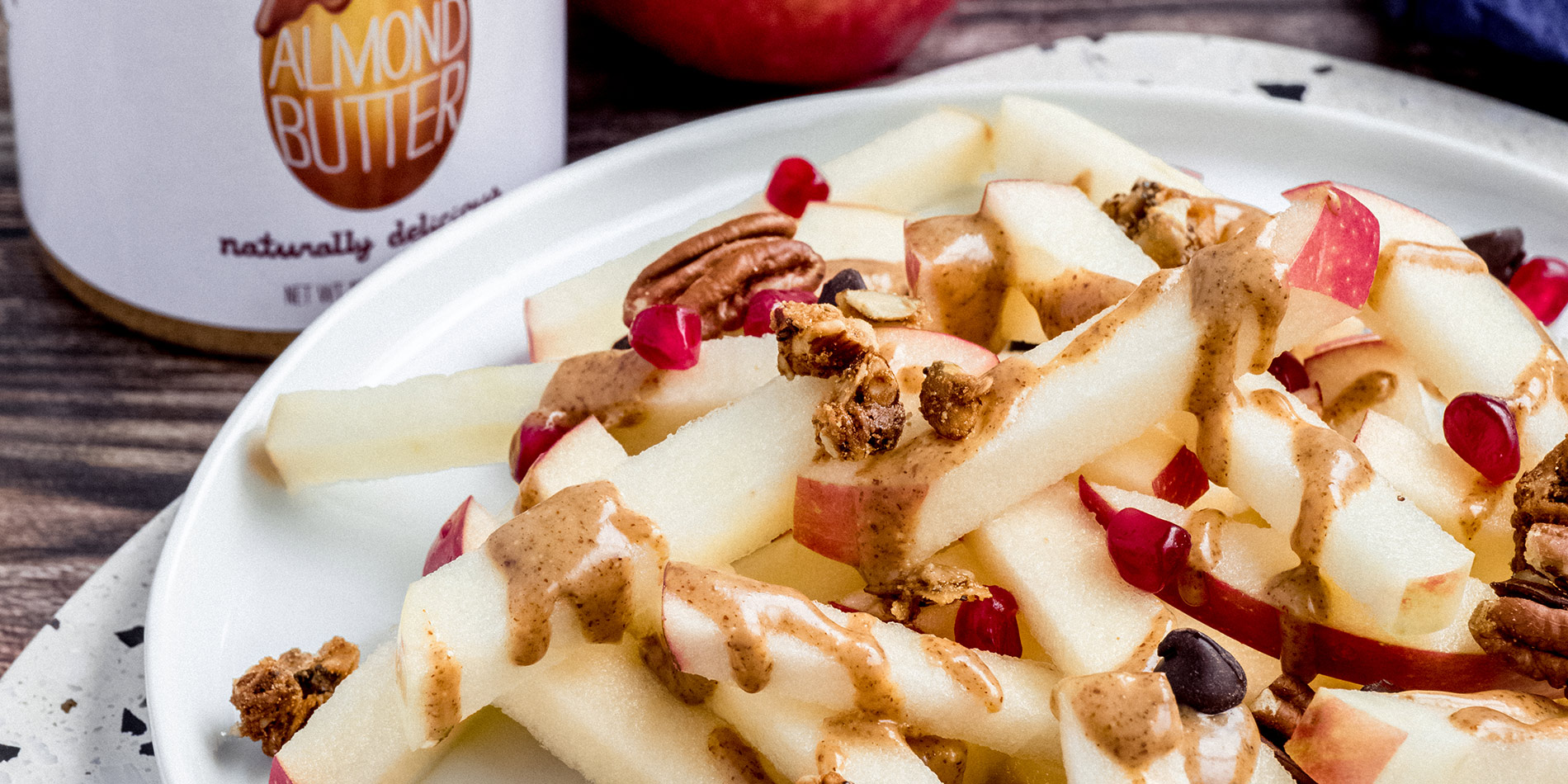 Apple Fries stacked on a ceramic plate, covered in Loaded dressing and toppings, on a dark wooden tabletop