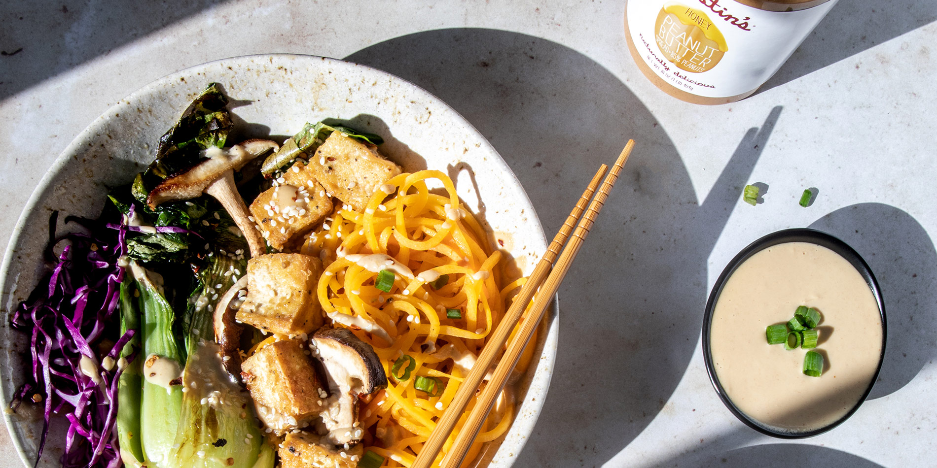 Peanut Miso Veggie Stiry Fry with chopsticks on a marbled plate and dipping sauce on a marbled countertop