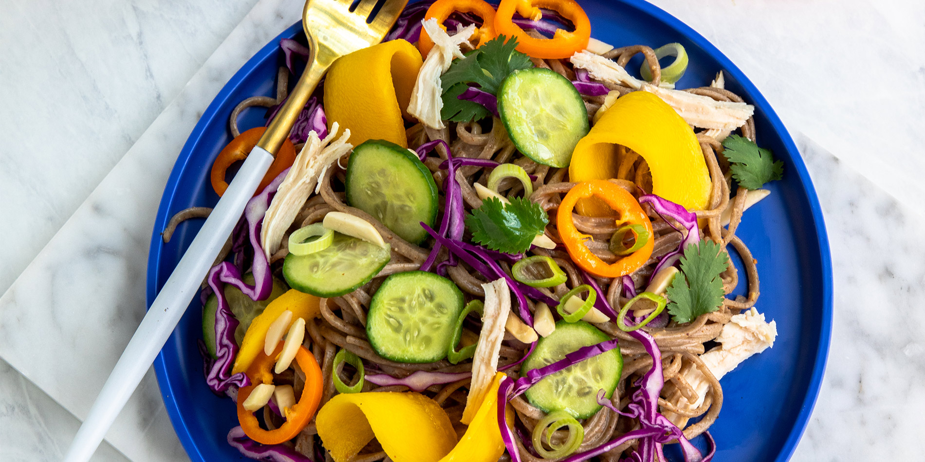 Summer Soba Salad on blue plate with a gold and white fork set on a marble countertop