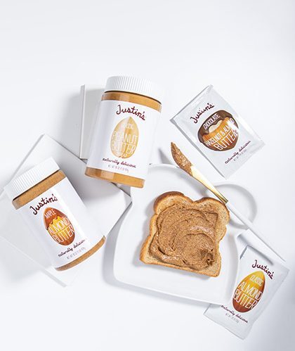 Justin's nut butter jars and spread pouches placed beside toast on white dish in a white background with white fabric