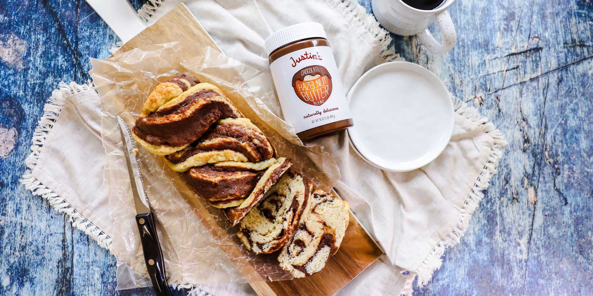 Chocolate Hazelnut Babka on a wooden serving board on a cloth beside a cup of coffee on a blue wood background